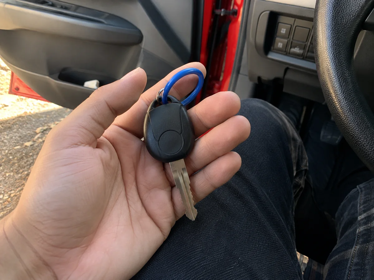 Compact car key with a blue keyring held beside a red car