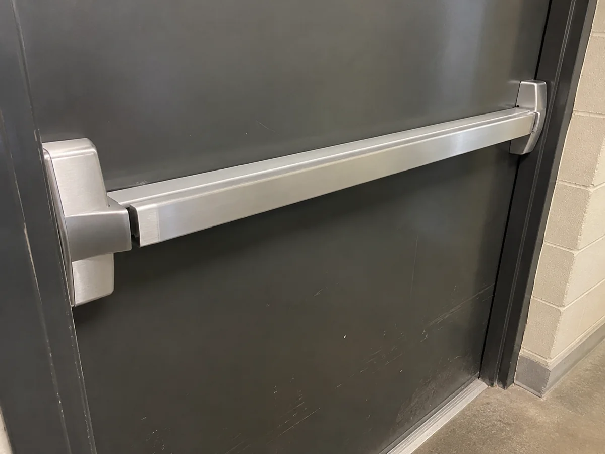 Silver exit push bar on a charcoal metal door