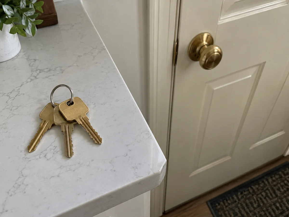Three brass house keys on a white kitchen counter