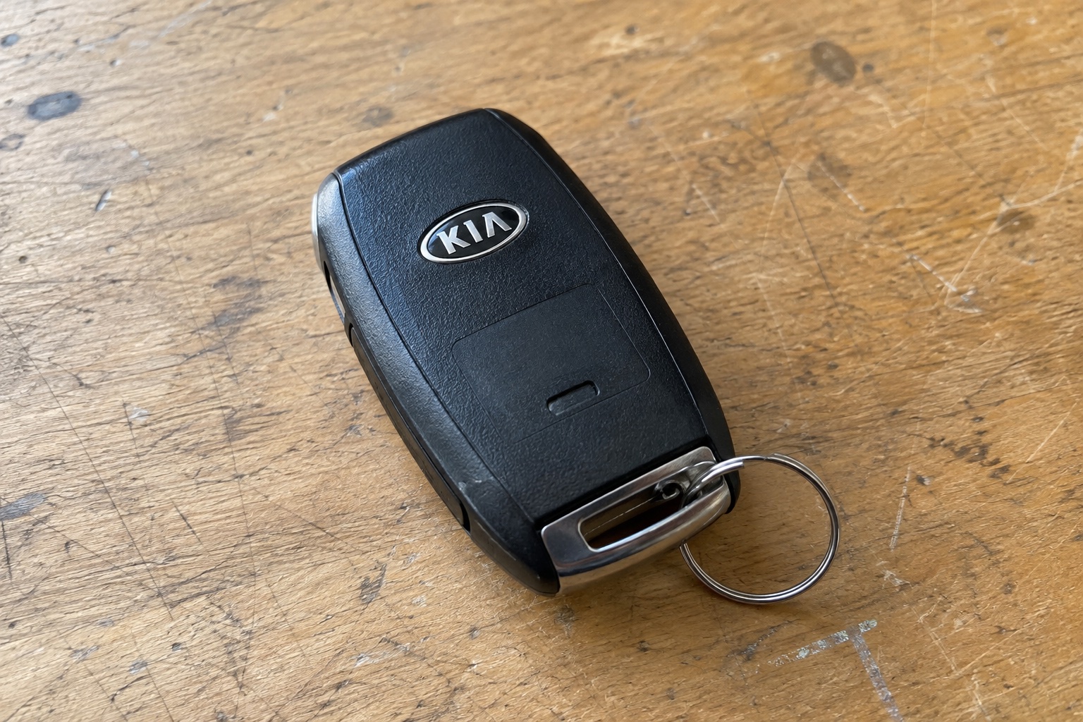 AI-generated illustration of a black key fob with an older Kia oval emblem on a wooden bench.